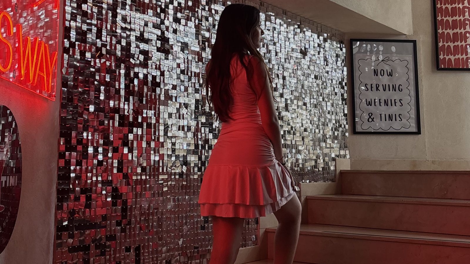 A woman in a red dress on stairs in front of a sequin wall