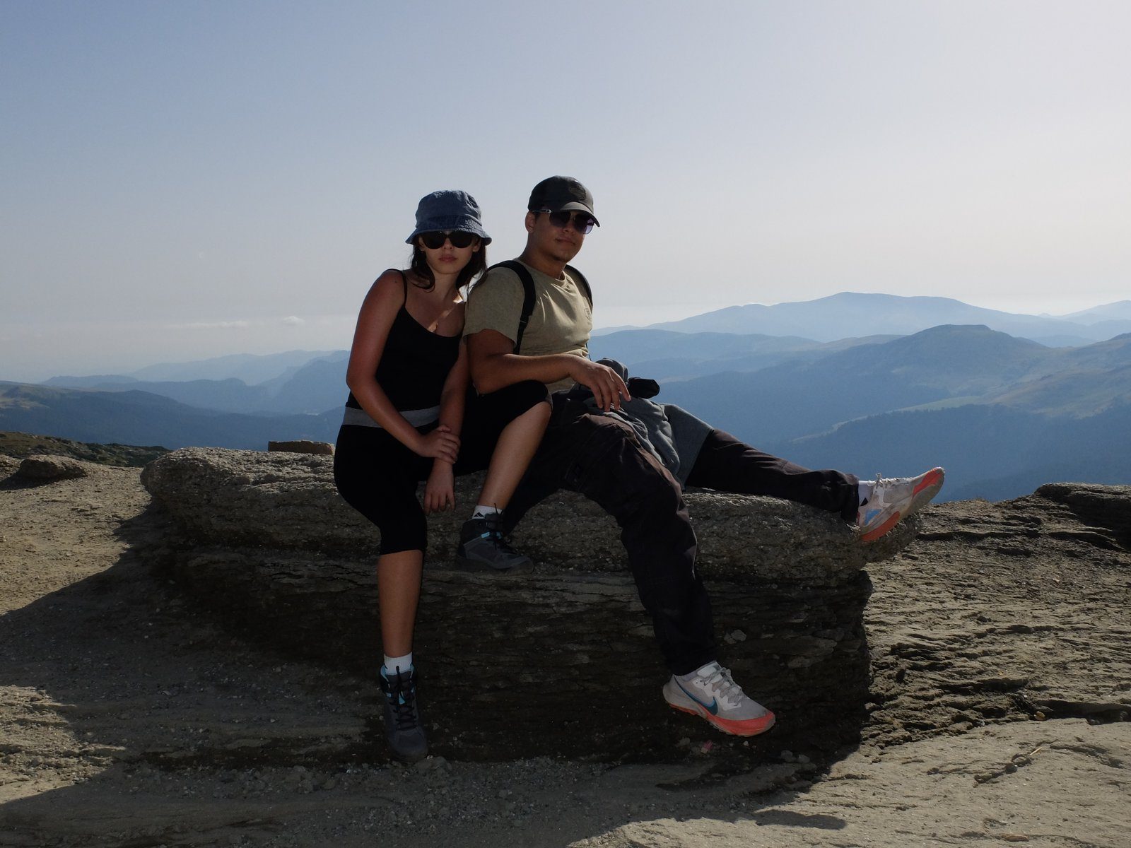Two hikers sitting on a rock above the mountains
