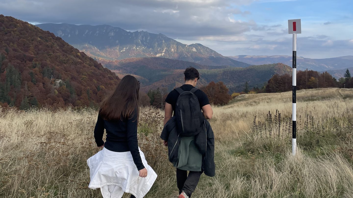Two hikers walking past a trail marker in autumn